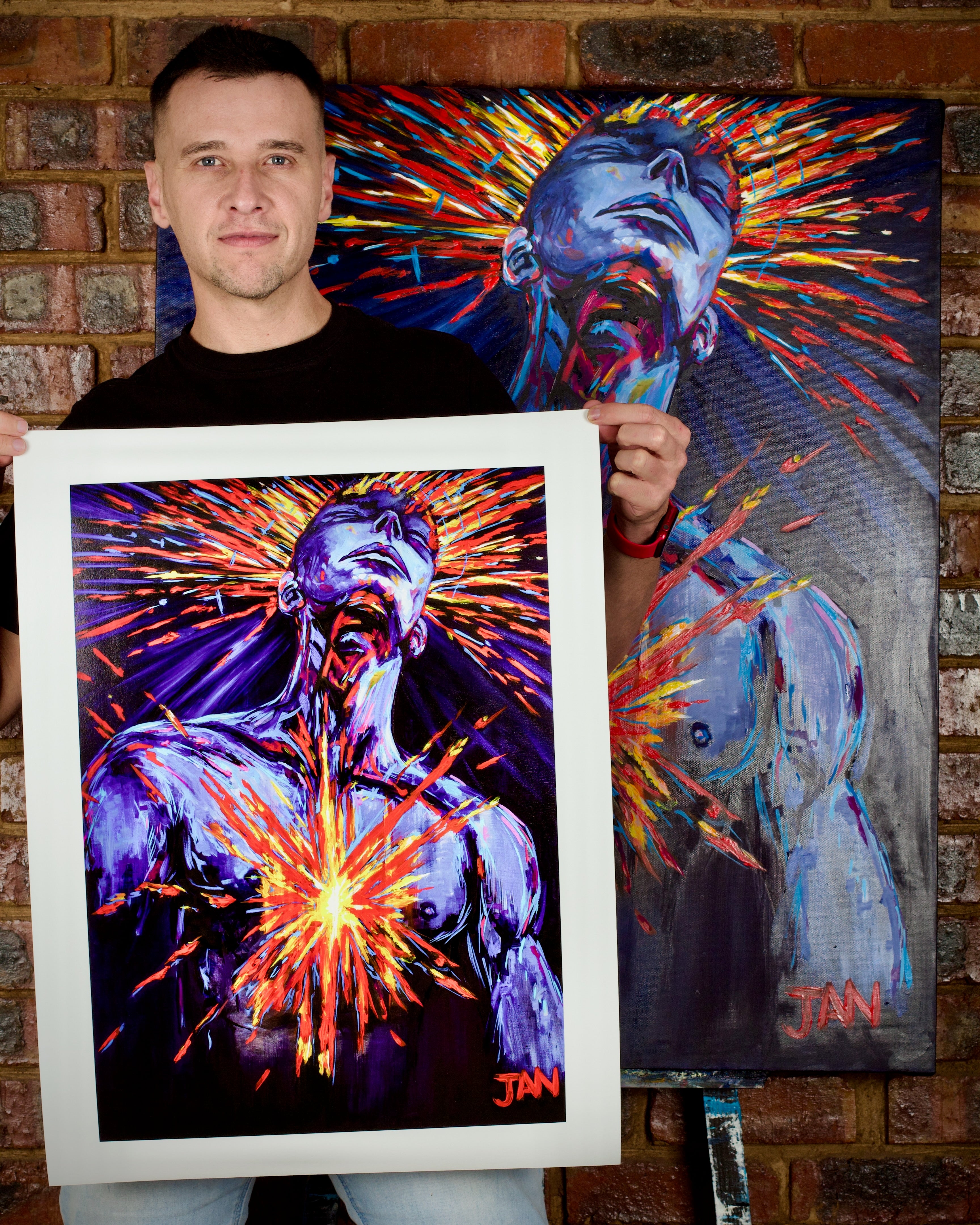 JAN holding a framed painting of a colorful abstract design with a brick wall background